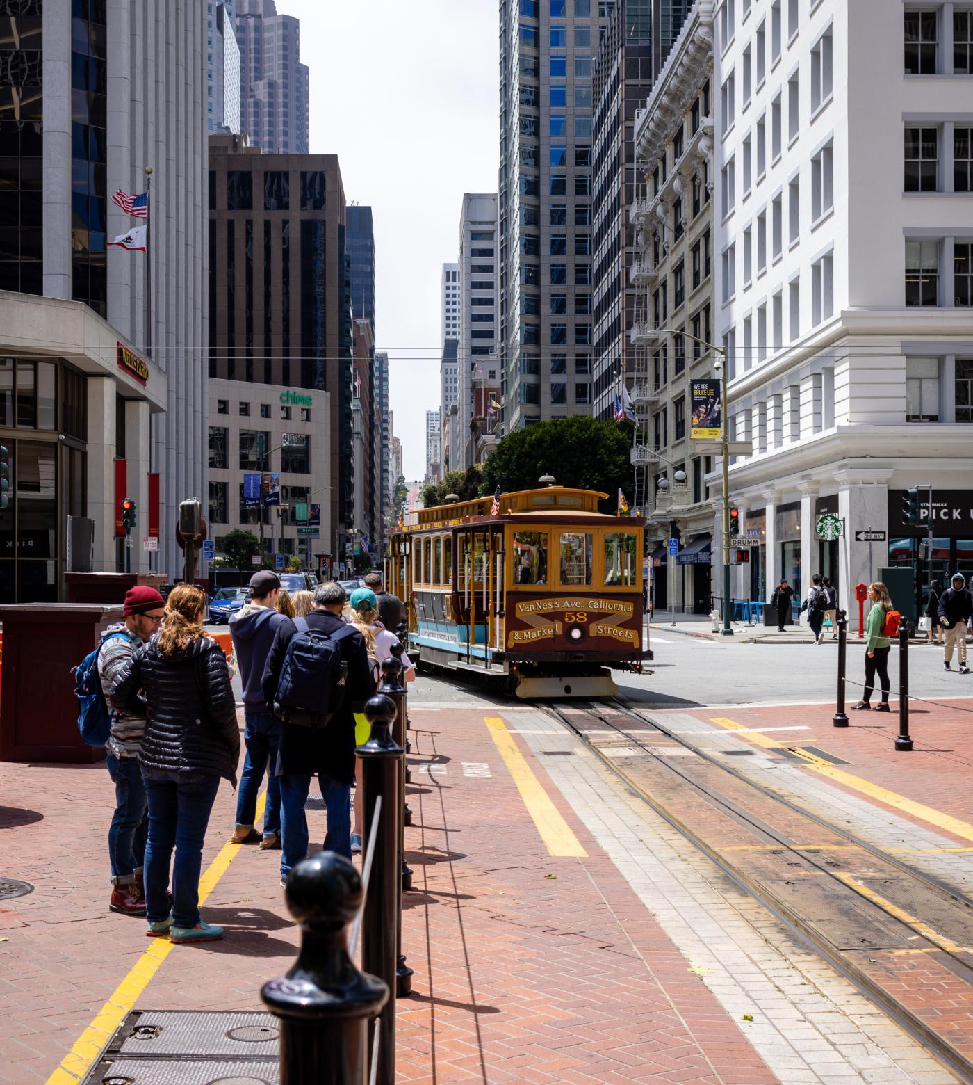 Group of people waiting on the street for an SF trolley to arrive.